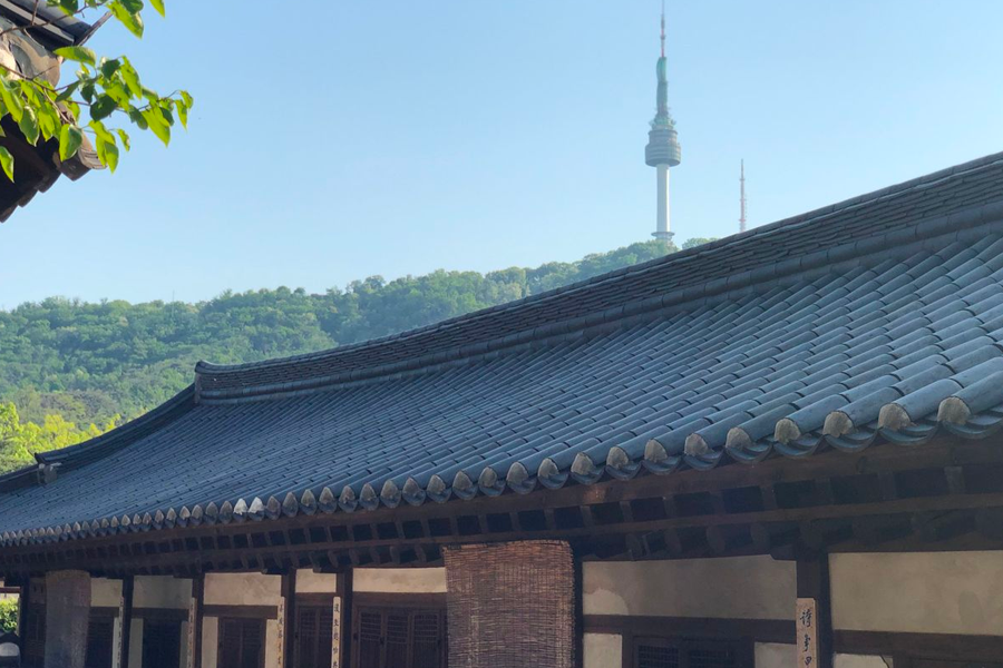 Namsan Seoul Tower seen from behind the tiled roof of a traditional Korean house in Namsan Hanok Village.