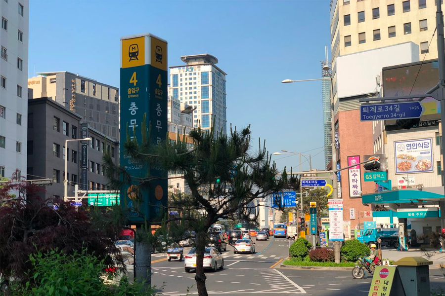 Street view outside Chungmuro Station Exit 4 towards Namsan Hanok Village, with buildings, traffic, and a clear sky above.