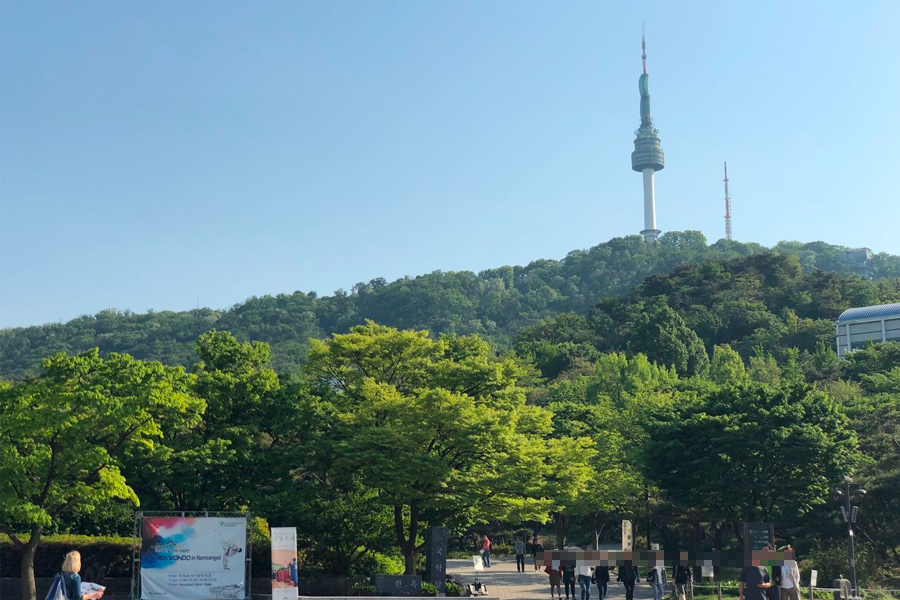 View of Namsan Seoul Tower from Namsan Hanok Village, surrounded by lush greenery under clear skies.
