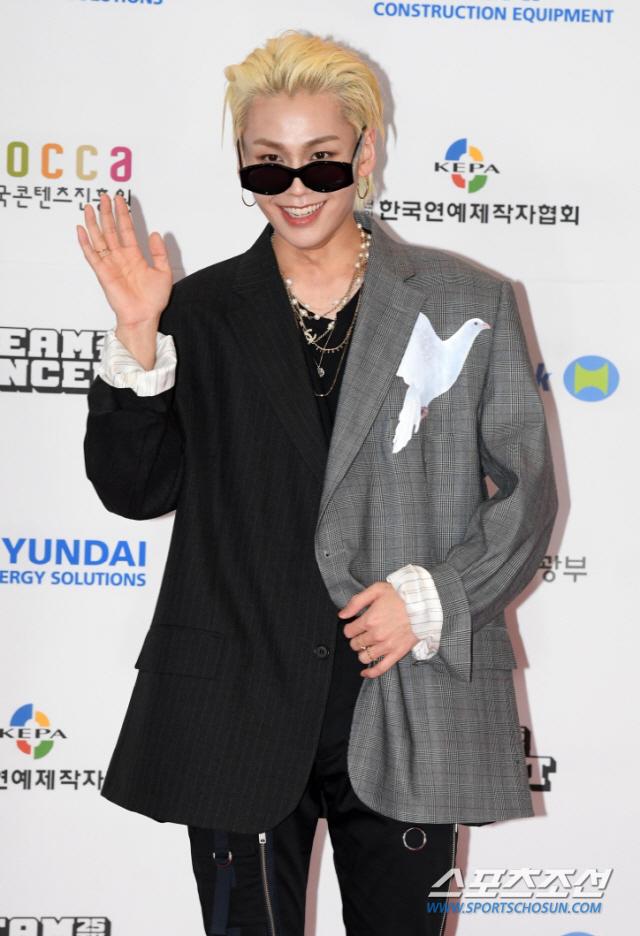 灰色と黒のコートを着て片手を挙げる男性（スポーツ朝鮮のイベントにて）