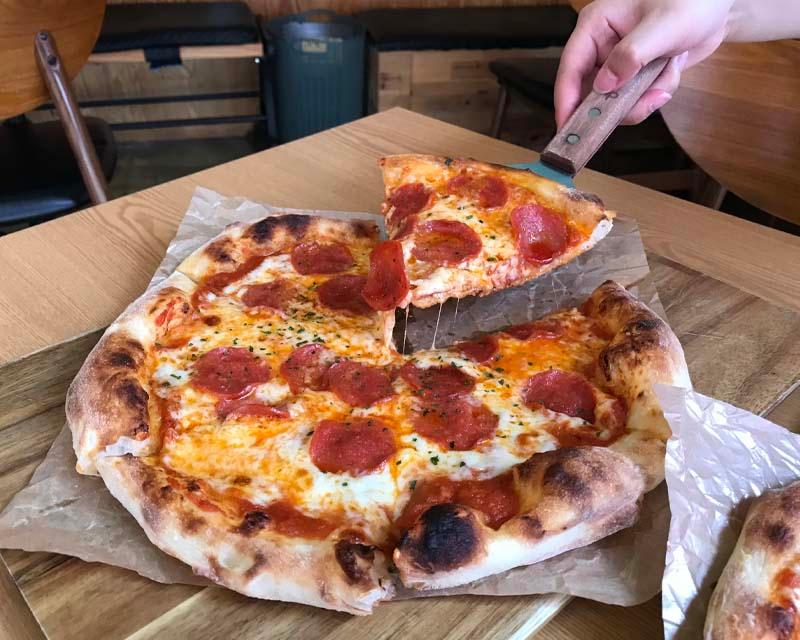 17 Pizza의 페퍼로니 피자 조각을 집어드는 모습. 치즈와 피자 도우의 조화가 인상적이다.