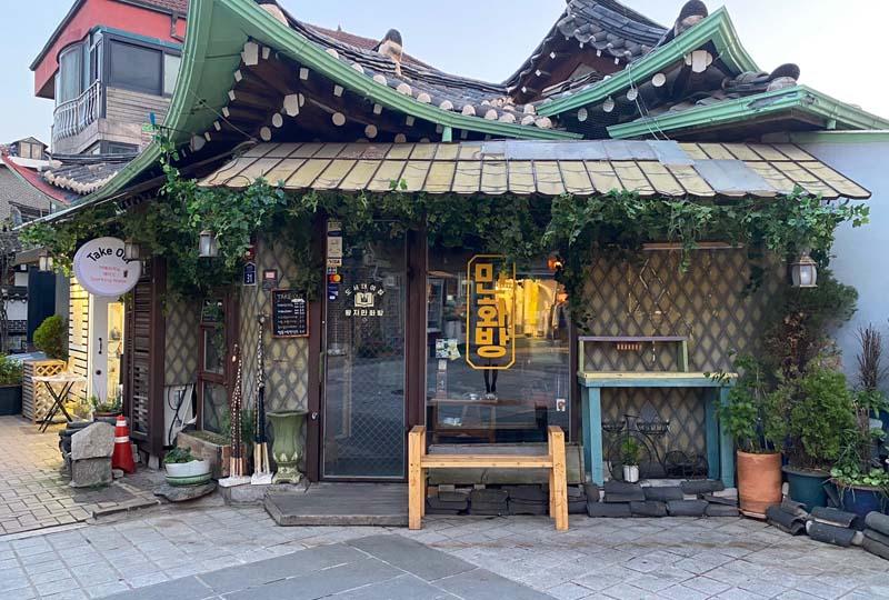 伝統的な韓国建築スタイルのカフェ。屋根には曲線があり、前景にはカフェの外装が見えます。カフェは都会の街並みに溶け込んでいます。