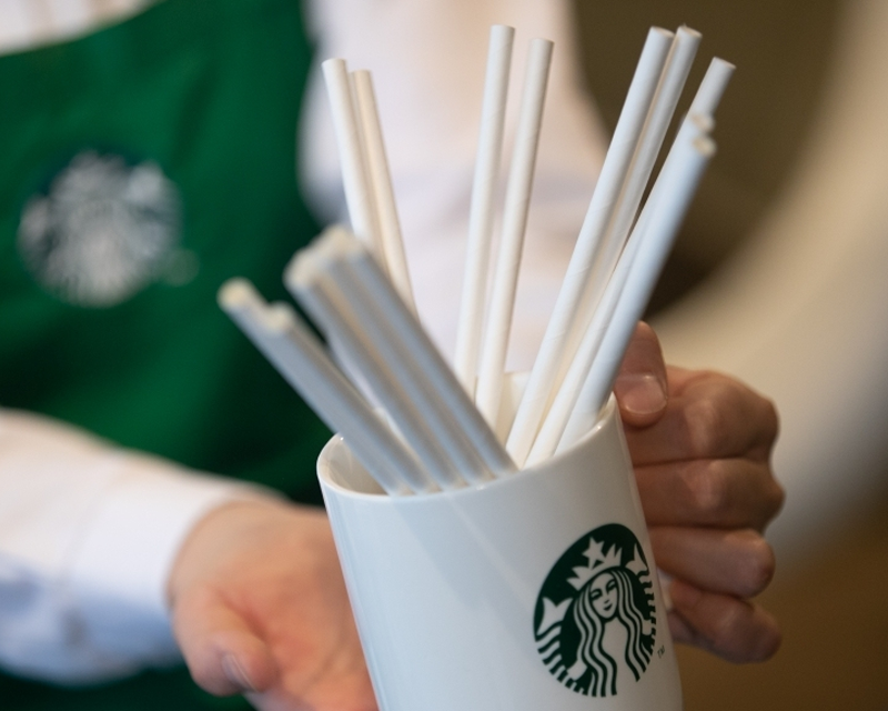 Barista sedang memegang gelas berlogo Starbucks yang berisi sedotan kertas putih, inovasi ramah lingkungan untuk mengurangi penggunaan plastik.
