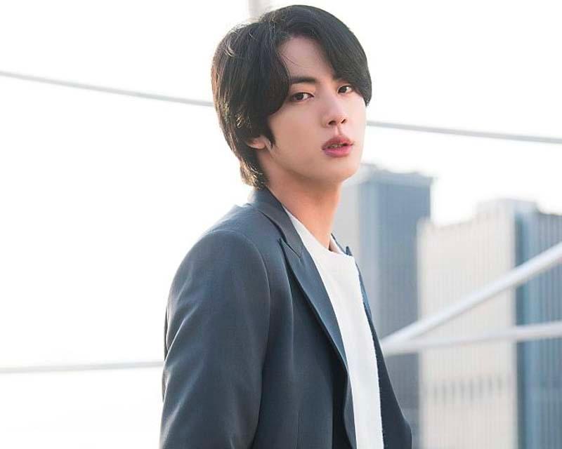 จิน BTS ในสูทสีเข้มกับเสื้อเชิ้ตสีขาวและเนคไทภาพถ่ายในบรรยากาศเปิดกว้าง