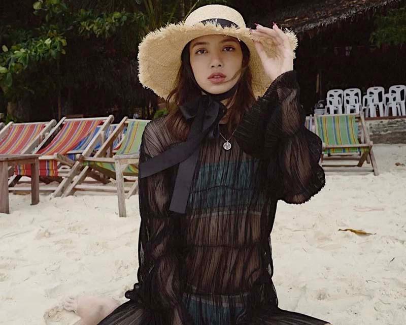 หญิงสาวในชุดซีทรูสีดำสวมหมวกปีกกว้างขนาดใหญ่ นั่งอยู่บนหาดทราย สไตล์เซ็กซี่และรักษ์โลก