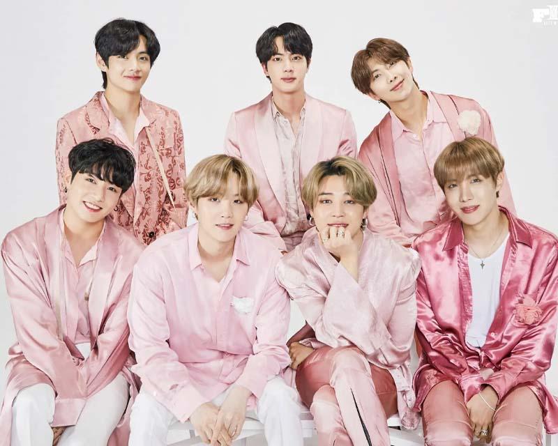 一組韓國男團的合照，成員們穿著休閒風格的服裝，站在簡單的背景前合影。