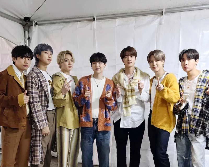 韓國男團合影，成員們身著華麗的舞台服裝，背景為舞台幕布，展現演出時的風采。