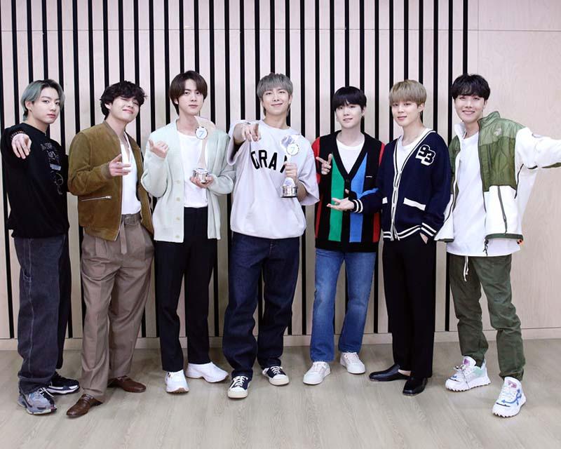 一組韓國男團的合照，成員們穿著粉色西裝，背景是粉色，展現甜美風格。