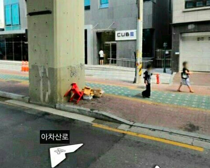 CUBE Entertainment 大樓的入口，寬敞的人行道上行人走過，紅色塑膠椅靠著路邊的水泥柱。