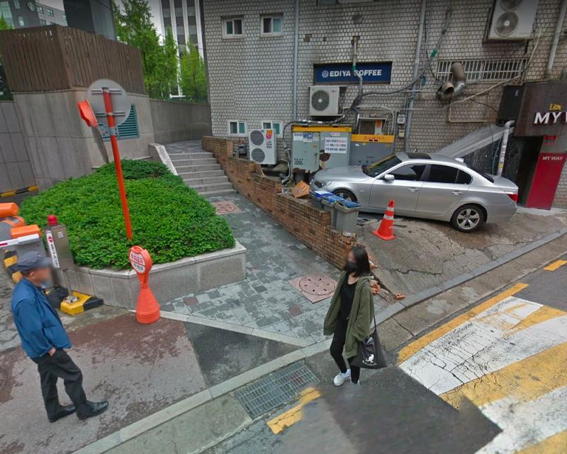 一位穿著深綠色夾克的女性，走過城市的人行道，非常接近停放和維修用的汽車。