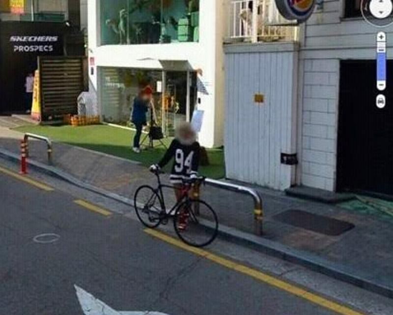 位於城市街道的自行車停在路肩側，一位戴運動帽的女士慢慢行走，她穿著印有數字“94”設計的黑色運動上衣。