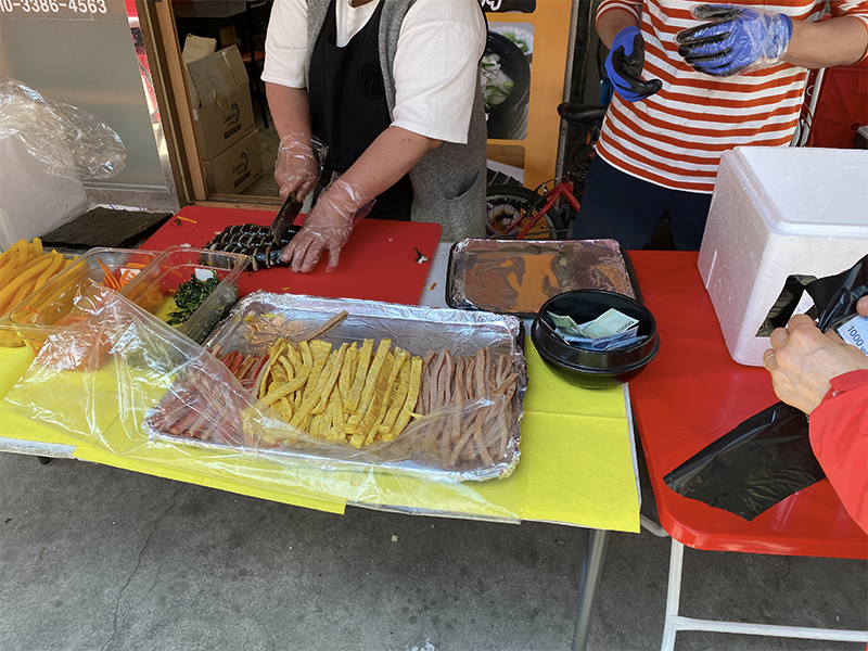 在地攤上售賣的韓式紫菜包飯及其準備過程，顯示了生動的韓國街頭美食文化。