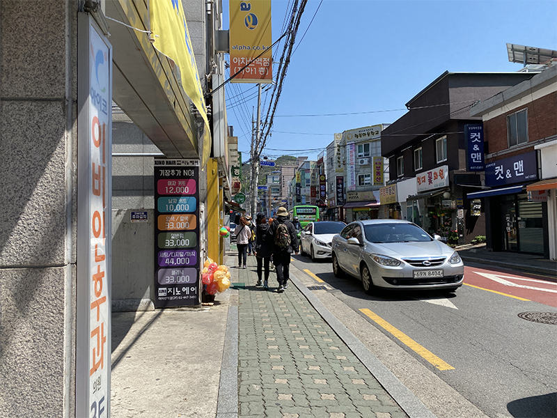 韓國都市街道間的片段，一車而過的人行道旁，標誌著忙碌的都市交通。