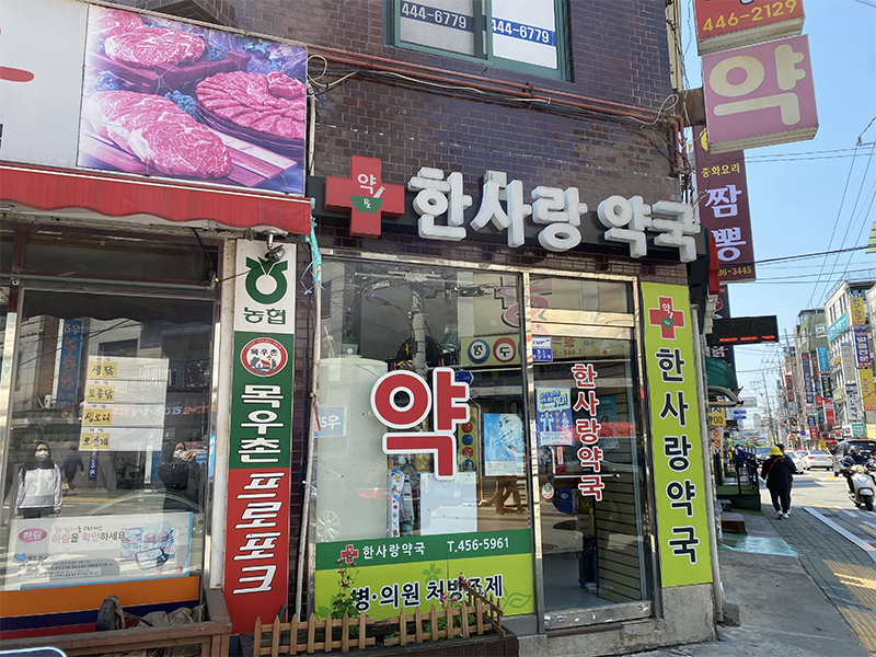 韓國典型街景，藥房和商店林立，街道上的行人展示了日常的繁忙生活。