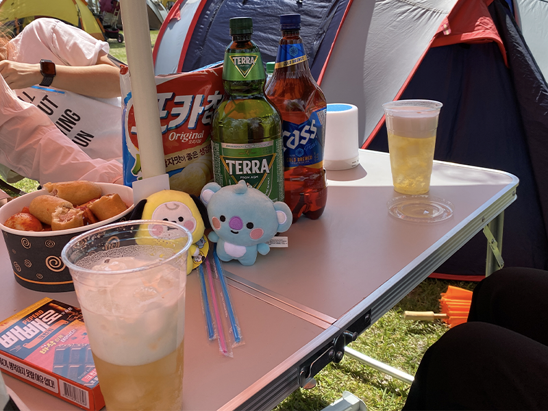 A table with plastic glasses of beer, bottles of beer and food on top