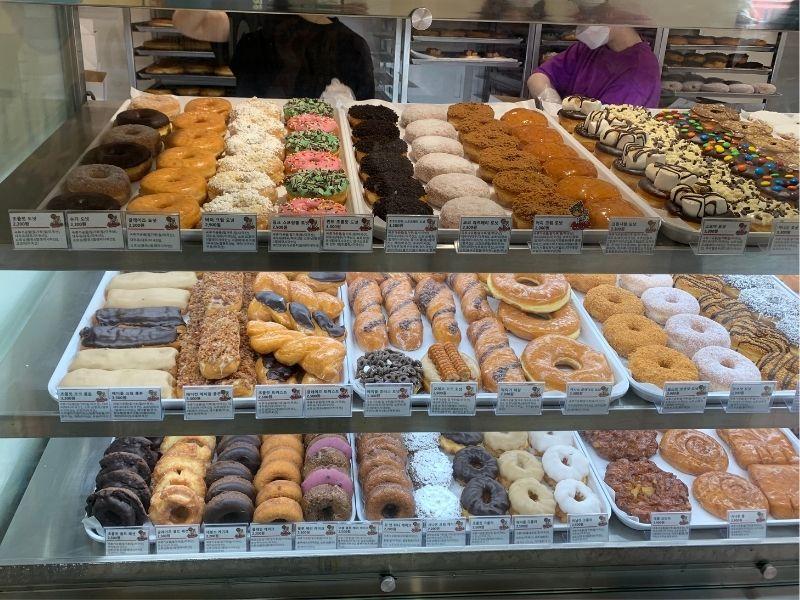 Kunde beim Aufgeben der Bestellung an der Kasse von Randy's Donuts, bei einer großen Auswahl an Donuts zur Auswahl.