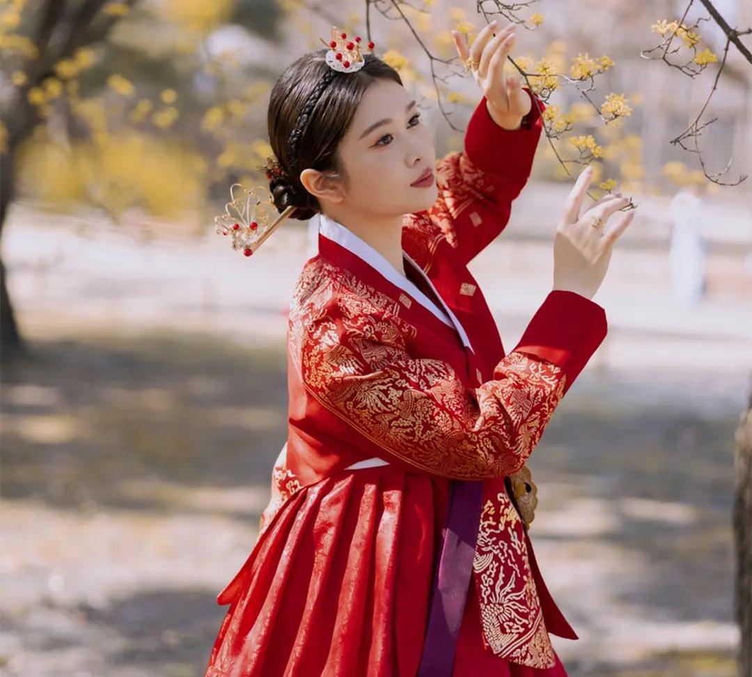 身穿華麗紅色傳統韓服的遊客在景福宮外庭與黃花互動，展示髮飾與細緻刺繡，呼應文章介紹的韓服免費入場與夜間拍照氛圍