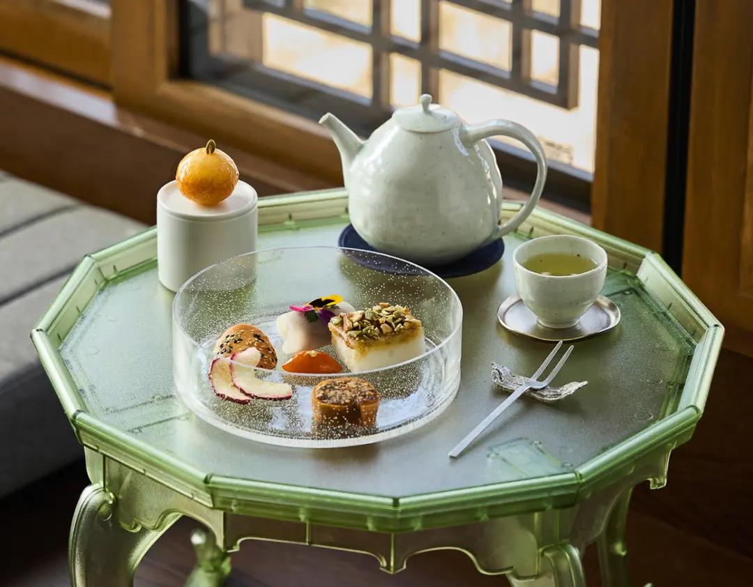 在韓屋窗邊的綠色八角小桌上擺著茶壺、茶杯與一盤韓式傳統點心，光線透過窗格營造溫暖、寧靜的韓宮風茶點氛圍，適合景福宮夜間行程推薦與體驗介紹。