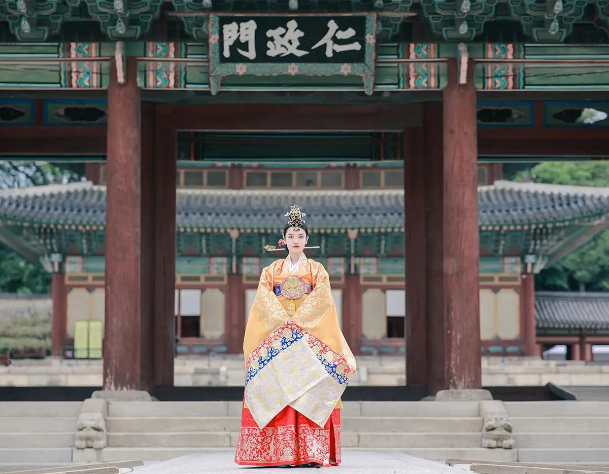 穿著華麗傳統韓服的旅客站在景福宮仁政門台階前拍照，色彩鮮豔的宮廷服裝與古老木構建築細節呈現濃厚的韓國古宮氛圍，適合夜間點燈行程介紹。