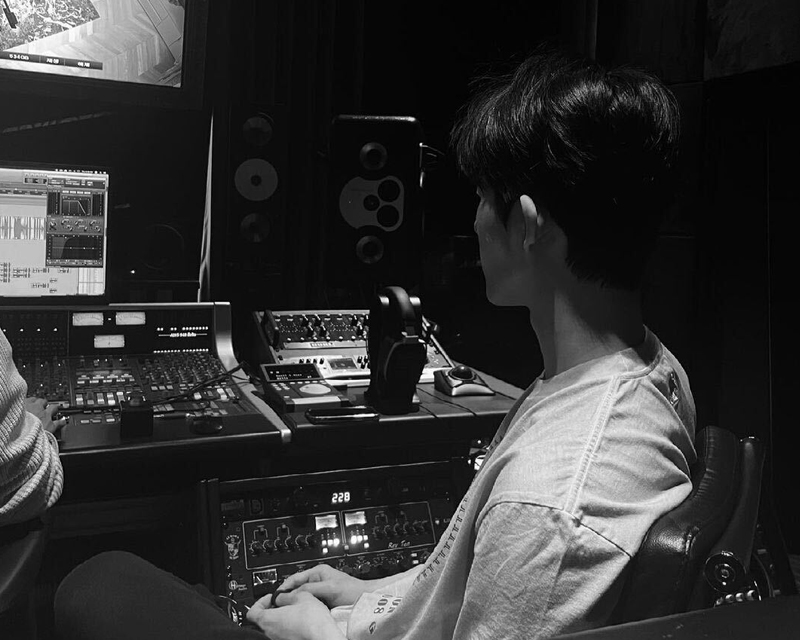 B.I อยู่ภายในสตูดิโอ บริเวณที่มีอุปกรณ์บันทึกเสียงและหน้าจอโทรทัศน์แสดงผลขณะทำงานในสตูดิโอ