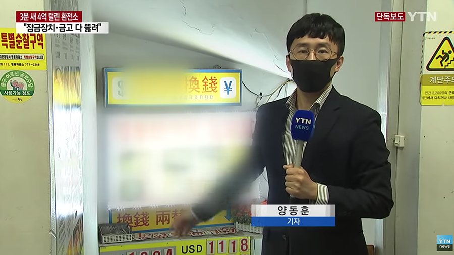 记者在韩国明洞一品香换钱所前进行新闻报道，背景中显示兑换率信息和“特别商品”的标志。
