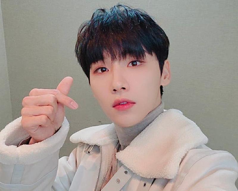 AB6IX田雄穿著毛茸茸的白色外套，用手比出愛心手勢，背景樸素。