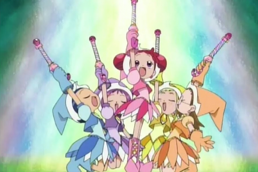 動畫中五位魔法少女團隊高舉魔法杖,背景泛著夢幻而多彩的光輝,角色們穿著各色魔法服裝展現活力。