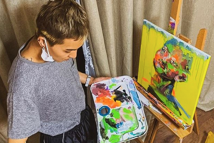 一位藝術家正在進行繪畫創作,手中持有調色盤,上面擠滿了豐富的顏料,背景中的畫架上是一幅鮮艷的人像作品。