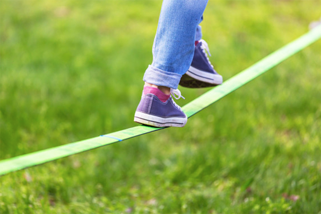 一名穿著牛仔褲的人正在公園裡走鋼索,專注於保持平衡,環境被綠色草地覆蓋。