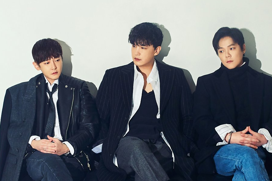 韓國樂團M.C the MAX的三位成員穿著正式服裝，並排坐在一起。