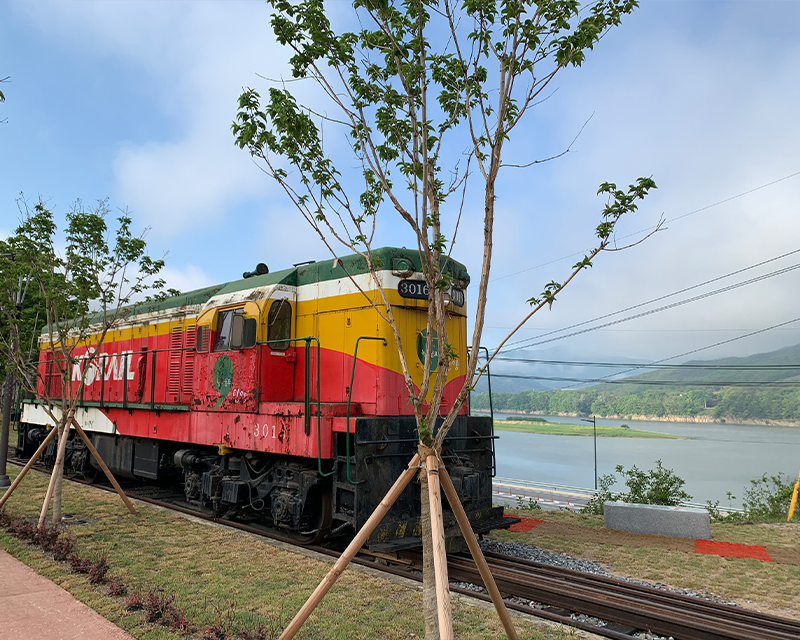 rusted red, green and yellow korail train car on tracks with namhan river and mountains in background near danyang station