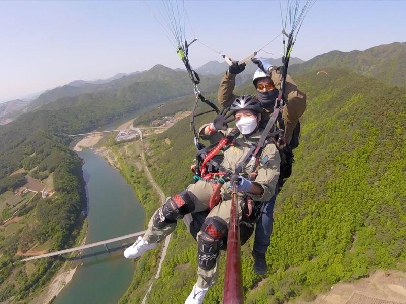 creatrip editor paragliding with expert and taking a photo with selfie stick with the landscape of danyang with moutains and river in the background
