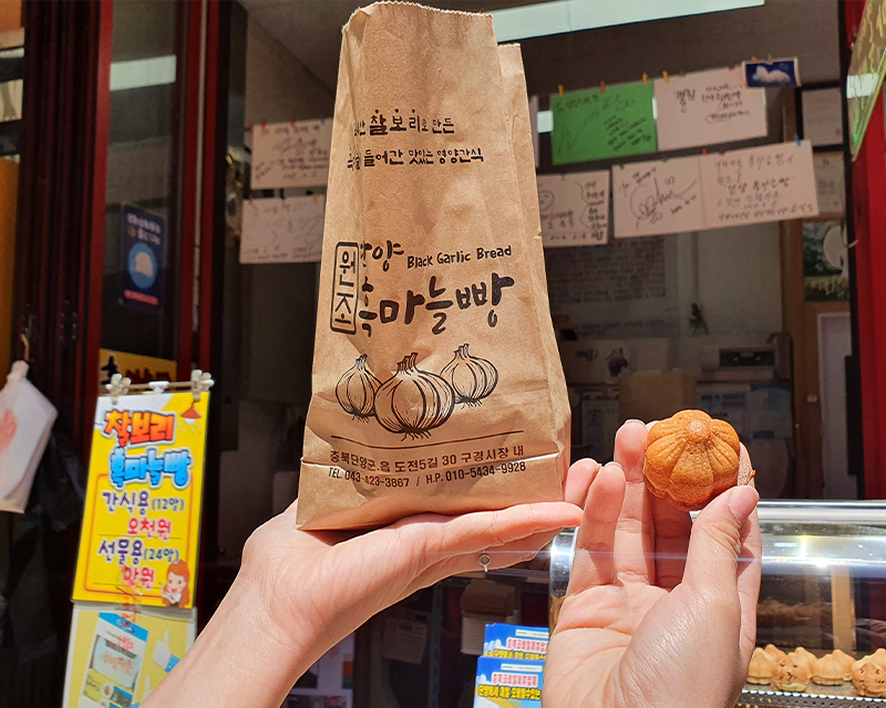 Black garlic bread paper bag and one bread held up in front of Black garlic bread stall at gugyeong market in danyang south korea