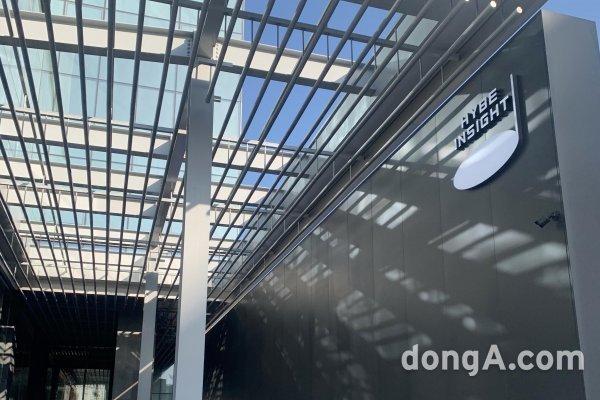  건물의 경사진 창문이 있는 HYBE 인사이트 외부 모습, 동아 제목이 포함되어 있음.