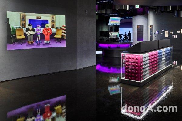  HYBE 인사이트 내부 모습, 애니메이션 영상이 벽에 투영됨, 왼쪽에는 조명 조명.