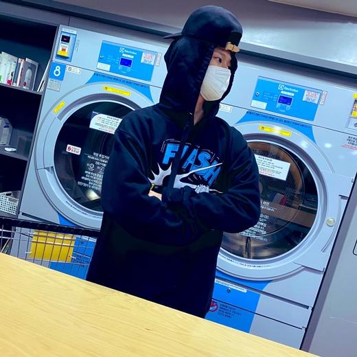 黒いフード付きジャケットを着て、ランドリールームでたたずむマルコの画像。リラックスした日のオフショット感を表現。