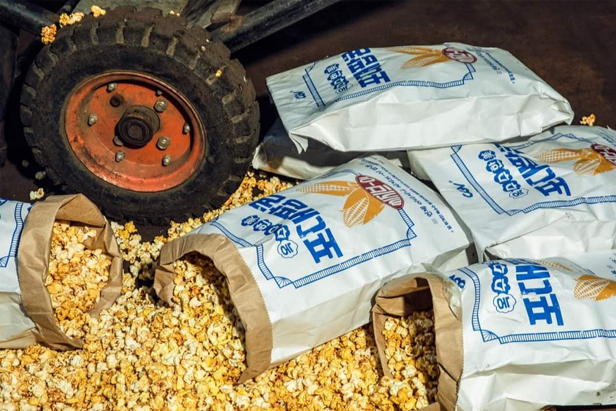大包的韩文包装袋，里面装满了新鲜的黄油爆米花，散落在地上，旁边有一个车轮。