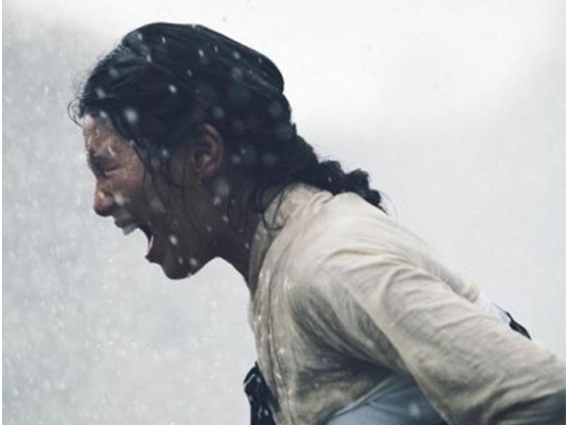 電影場景中的一位女性角色,背景下的大雨和造型展示了她心中深厚的恨意和情感壓抑。