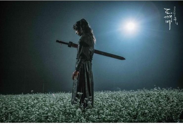 韓劇孤單又燦爛的神裡的場景,角色揚起劍站在花田中,周圍的風景和姿勢透露著恨."