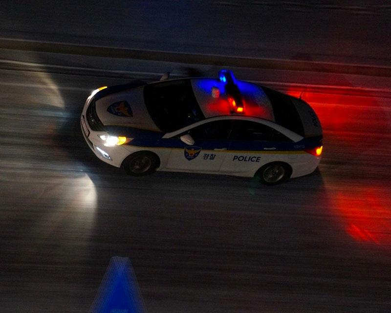 รถตำรวจวิ่งในยามค่ำคืนสะท้อนแสงไฟเขียวแดงบนถนน