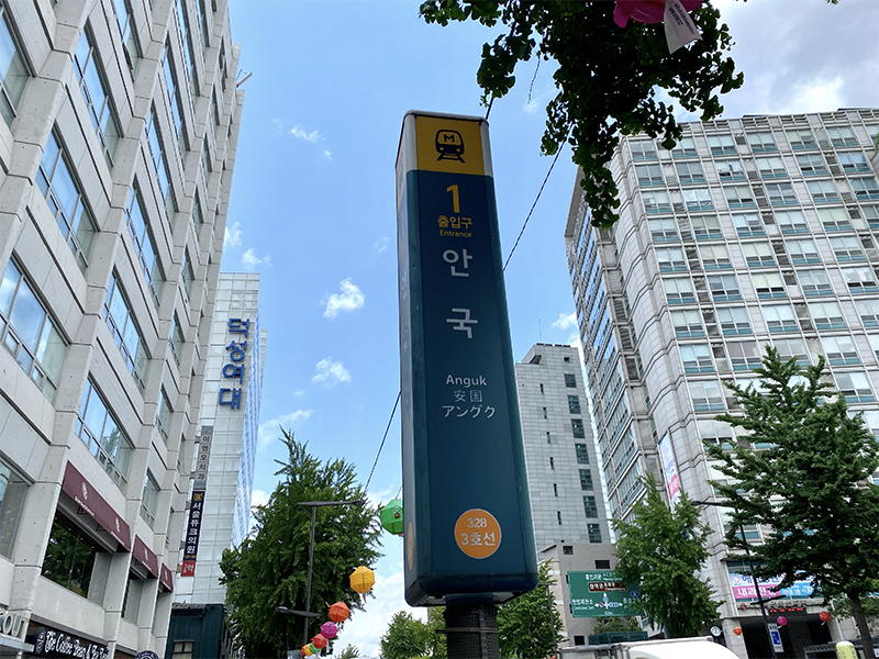 Anguk Station sign marking Exit 1, located amidst tall buildings on a clear day in Seoul.