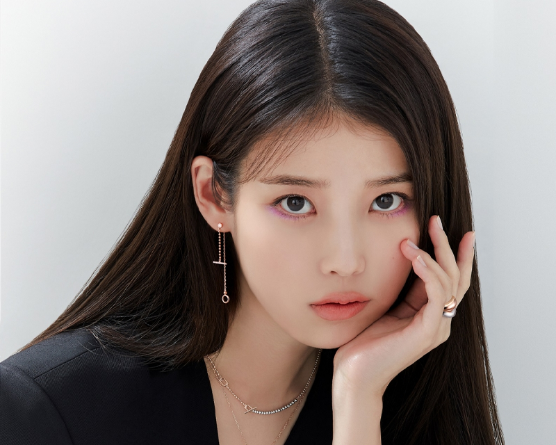 韓國藝人IU的照片，背景灰色，佩戴精緻耳飾和項鍊。