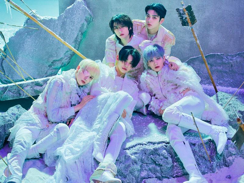 TXT วงบอยแบนด์จากเกาหลีในชุดสีขาว พวกเขานอนอยู่บนฉากที่ดูเหมือนท้องฟ้ายามค่ำคืน