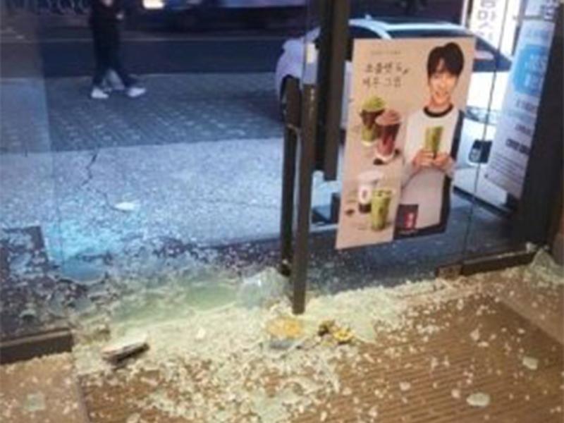 貢茶店面玻璃破碎，地上散落玻璃碎片，旁邊貼有李昇基的廣告海報，象徵避災的趣味情節。