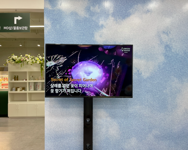 Schermo TV all'ingresso di Flowers By Naked a Hongdae che guida i visitatori attraverso le diverse zone espositive.