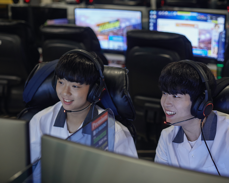 two Korean students wearing school uniform with headsets on playing games at PC bang