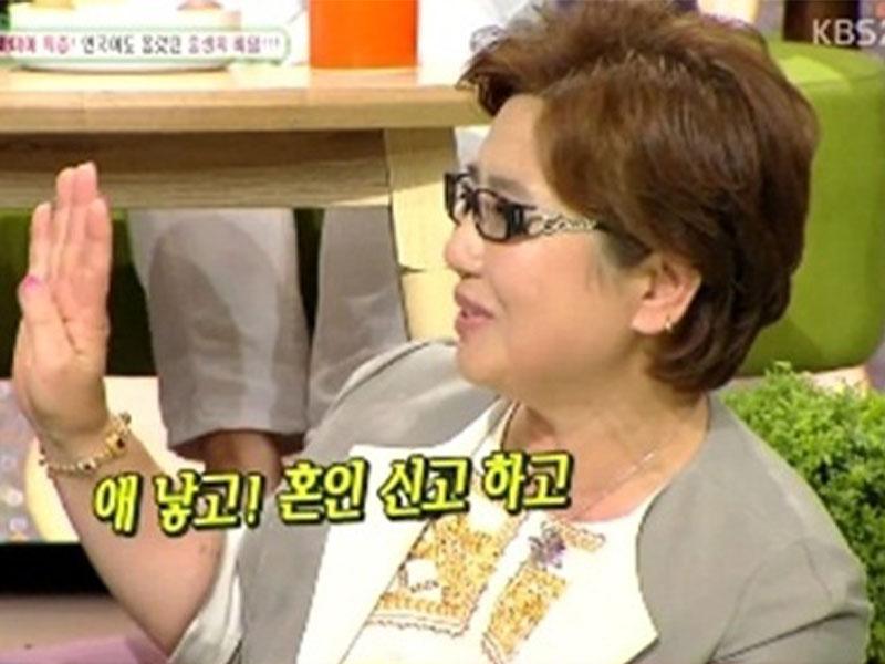 韓國綜藝節目場景，一名婦女在節目中抬手説話，背景有多彩的道具和字卡，有 KBS 字樣