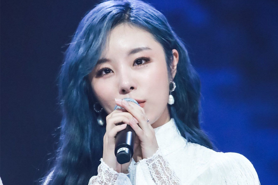 韩国女团MAMAMOO的成员之一,身着白色蕾丝连衣裙,在舞台上握着麦克风进行演唱。