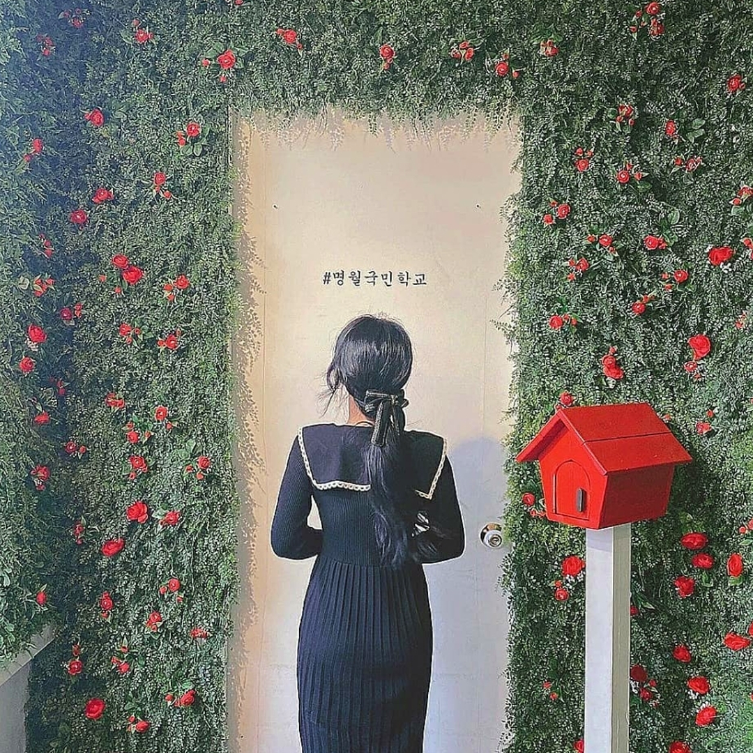 Girl in black dress standing infront of a wall with red flowers at Myeongwol Elementary School