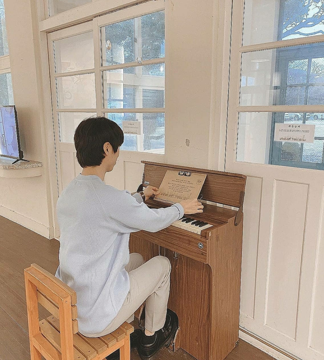 Boy sitting on a small wooden chair with a piano at Myeongwol Elementary School